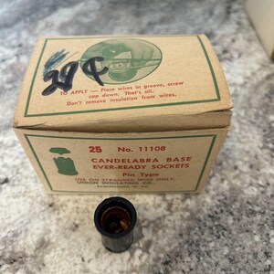 May include: A vintage cardboard box for candelabra base sockets, with the text "25 No. 11108 CANDELABRA BASE EVER-READY SOCKETS Pin Type". A black socket sits in front of the box. The box has green and red text.