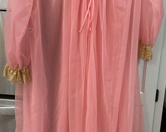 May include: A vintage pink chiffon nightgown with a delicate lace collar and cuffs. The nightgown features a tie closure at the neckline and a lace trim along the hemline. The sleeves are long and gathered at the wrist.