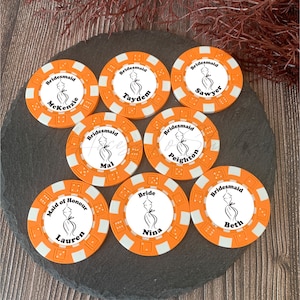 May include: Seven round orange and white poker chips featuring a central white circle with a black line drawing of a dress. The text includes Bridesmaid, Maid of Honour, or Bride, followed by names: McKenzie, Taydem, Sawyer, Mal, Peighton, Lauren, Nina, and Beth.