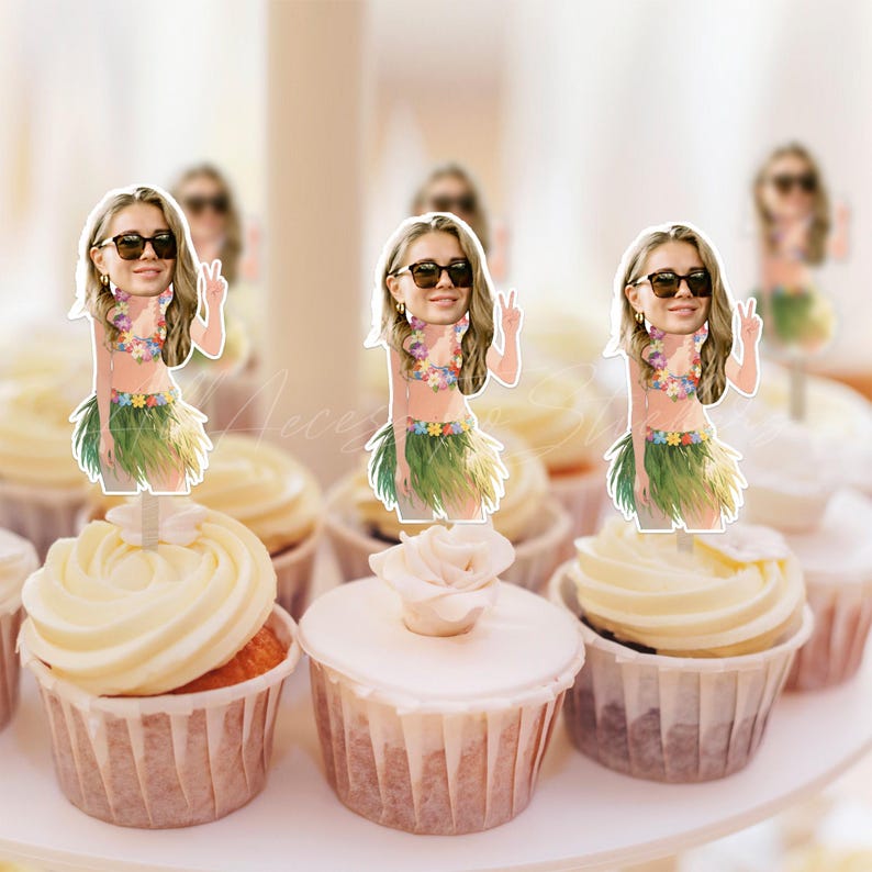 May include: Three cupcake toppers featuring a cartoon-style illustration of a person with long blonde hair, wearing dark sunglasses, a floral bikini top, and a green grass skirt, making a peace sign gesture, placed on frosted cupcakes.