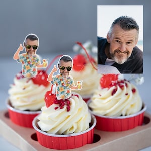 May include: A set of cupcakes in red paper liners topped with white frosting, red cherries, and custom cardboard cutouts featuring a cartoon illustration of a man with a beard and sunglasses wearing a floral shirt, alongside a reference photograph.