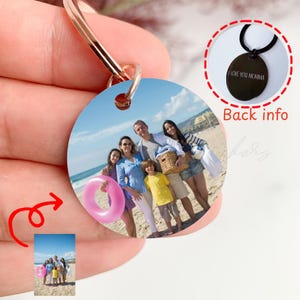 May include: A circular metal keyring featuring a printed photograph of a family on a beach. The keyring has a rose gold ring attachment. An inset shows the back of the circular pendant, which is black and engraved with the text I LOVE YOU MOMMA.