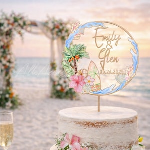 Op de afbeelding: Een ronde taarttopper met een houten frame en een aquarelontwerp van een palmboom, hibiscusbloemen, schelpen en blauwe golven. De tekst luidt Emily & Glen 05.24.2025. De topper is bevestigd op een enkele prikker bovenop een witte taart.