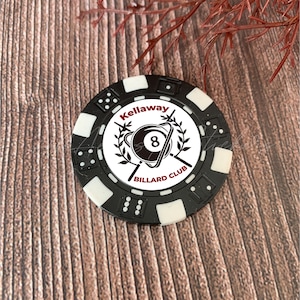 May include: A round black and white poker chip featuring a central graphic of an 8-ball surrounded by laurel branches and the text Kellaway BILLARD CLUB. The outer edge of the chip is decorated with small dice patterns in alternating black and white.