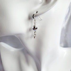 May include: A single silver earring with a disco ball charm and a small star pendant. The earring is suspended from a curved hook, showcasing a playful and eye-catching design. The disco ball reflects light, adding a touch of sparkle.