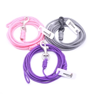Può includere: Tre guinzagli per cani in rosa, grigio e viola, ciascuno arrotolato e con un moschettone in metallo. I guinzagli hanno una consistenza simile a una corda e includono un'etichetta bianca con la scritta "INNERSINE IT'S A VIBE".