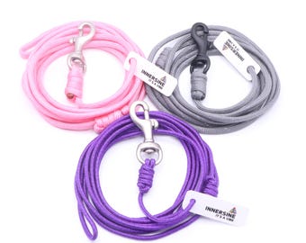 May include: Three dog leashes in pink, gray, and purple, each coiled and featuring a metal clasp. The leashes have a rope-like texture and include a white tag with the text "INNERSINE IT'S A VIBE".