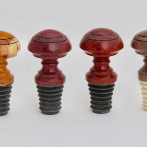Può includere: Quattro tappi per bottiglie in legno con diversi motivi e colori di venatura del legno. I tappi hanno una base nera, rossa, marrone e bianca.