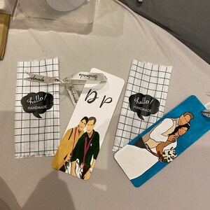 May include: Three handmade bookmarks with different designs. One bookmark features a couple in a wedding setting, another bookmark features a couple with a dog, and the third bookmark has the word "b&p" written on it.