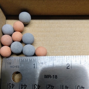 May include: A close-up of a group of small, round, ceramic beads in gray and orange colors. The beads are arranged in a triangular shape and are measured against a ruler with inch markings.