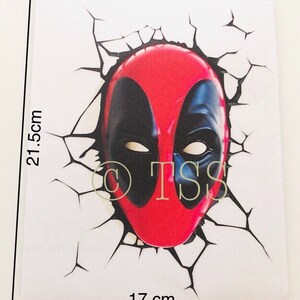 May include: A red and black Deadpool mask graphic sticker with a cracked wall effect. The sticker is 17 cm wide and 21.5 cm tall.