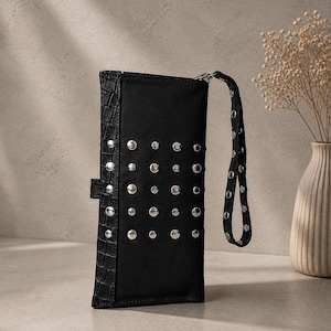 May include: A black rectangular clutch wallet featuring a vertical panel with a textured crocodile-embossed pattern and a main section adorned with a grid of silver-toned metal studs. The wallet includes a matching wrist strap with silver studs.