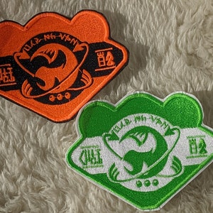 May include: Two embroidered patches, one orange and one green, with a black and white design of a creature with wings and a planet. The text on the patches reads "OLD -  NEW -  VINTAGE" and "CHAT".