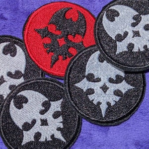May include: Five embroidered patches with a skull and wings design. Four patches are black with a silver skull and wings design. One patch is red with a black skull and wings design.