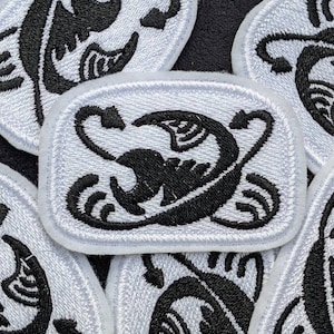 May include: A set of five white embroidered patches with a black scorpion design. The scorpion is stylized and has a curled tail.