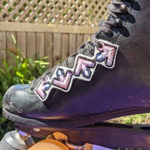 May include: Black roller skates with pink and blue arrows on the side. The skates have a black leather upper and a white sole.