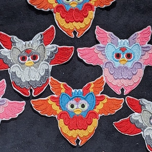 May include: Six embroidered iron-on patches featuring colourful cartoon characters with wings. The characters have different coloured fur, eyes, and wings. The patches are perfect for adding a fun and whimsical touch to clothing, bags, or other fabric items.