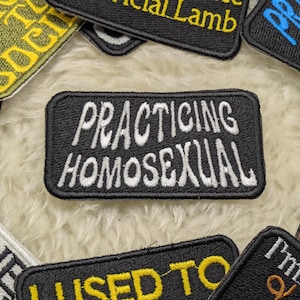 Puede incluir: Un parche bordado negro con texto blanco que dice "Practicing Homosexual".