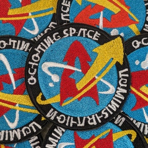 May include: Close-up of several embroidered patches with a blue background, white and yellow accents, and the text "OCHO-TIMI LING SPACE", "OCHO-TIMI LING", and "OCHO-TIMI LING" visible.