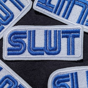 May include: Four white patches with blue embroidered lettering. The word "SLUT" is spelled out in large letters on one patch.