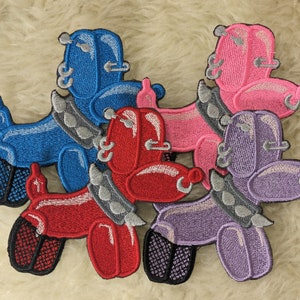 May include: Four embroidered iron-on patches of balloon animal dogs in blue, pink, red, and purple. Each dog has a silver chain collar with spikes and multiple silver rings on its body.