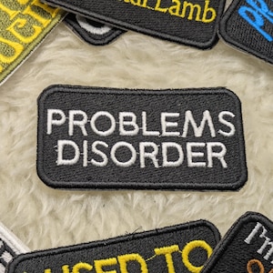 May include: Black embroidered patch with white text that reads "PROBLEMS DISORDER".