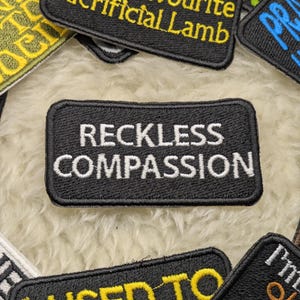 Peut inclure: Patch brodé noir avec du texte blanc qui dit "Reckless Compassion".