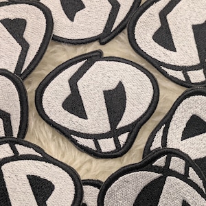 Op de afbeelding: Een verzameling witte geborduurde strijkpatches met zwarte schedelontwerpen. De schedels hebben een eenvoudig, cartoonachtig ontwerp met een brede grijns.