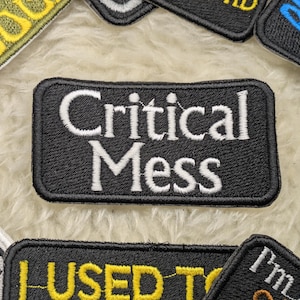 May include: Black and white embroidered patch with the text "Critical Mass" in white lettering.