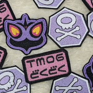 Peut inclure: Un ensemble de patchs thermocollants brodés représentant un monstre violet et noir aux yeux jaunes, un motif de crâne et d'os croisés, ainsi que le texte "TMOG どくどく".