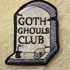 May include: A grey embroidered patch shaped like a tombstone with the text "Goth Ghouls Club" and a small skull at the bottom.