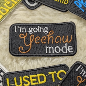 May include: Black iron-on patch with white and orange embroidery. The patch reads "I'm going Yeehaw mode".