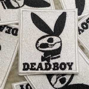 Peut inclure: Patch brodé blanc avec une silhouette de lapin noir portant des lunettes de soleil et un nœud papillon. Le texte "DEADBOY" est sous le lapin.