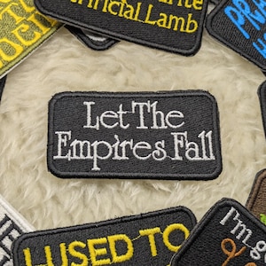Peut inclure: Écusson brodé noir avec du texte blanc qui dit "Let The Empires Fall".