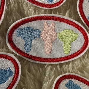 May include: Three embroidered patches with a red border and white background. The patches feature three different shapes in blue, pink, and green.