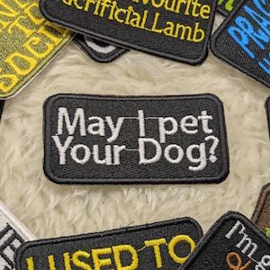 May include: A black and white embroidered patch with the text "May I pet Your Dog?" in white lettering. The patch is surrounded by other colourful patches with various text.