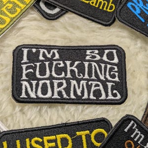 May include: Black and white embroidered patch with the text "I'm so fucking normal".