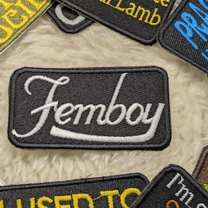 Könnte beinhalten: Schwarzer gestickter Aufnäher mit weißem Text, der "Femboy" lautet.
