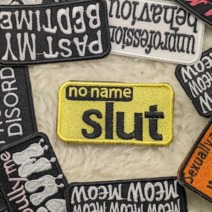 May include: A collection of embroidered patches with various phrases and words. The central patch is yellow with the word "Slut" in black. Other patches include phrases like "Past My Bedtime" and "Meow Meow Meow".
