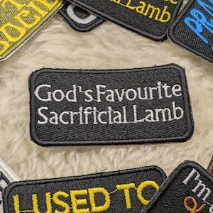 May include: Black and white embroidered patch with the text "God's Favourite Sacrificial Lamb".