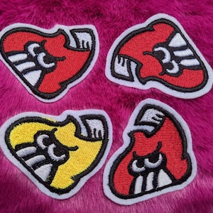 May include: Four embroidered iron-on patches in the shape of a heart. Two patches are red, one is yellow, and one is a darker red. Each patch has a white outline and black details.