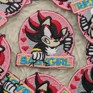 May include: Pink and black embroidered iron-on patch with a cartoon character and the text "Baby Girl".