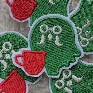 May include: Five green and white embroidered patches with a white design of a pair of glasses and a coffee cup. The patches are surrounded by a white border.