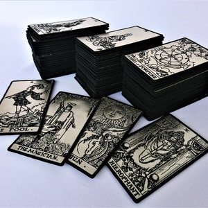 Könnte beinhalten: Ein Set schwarzer und silberner Tarotkarten mit Bildern von Der Narr, Der Magier, Die Sonne und Der Hierophant. Die Karten sind in einem Stapel gestapelt, wobei die oberste Karte das Rad des Schicksals zeigt.