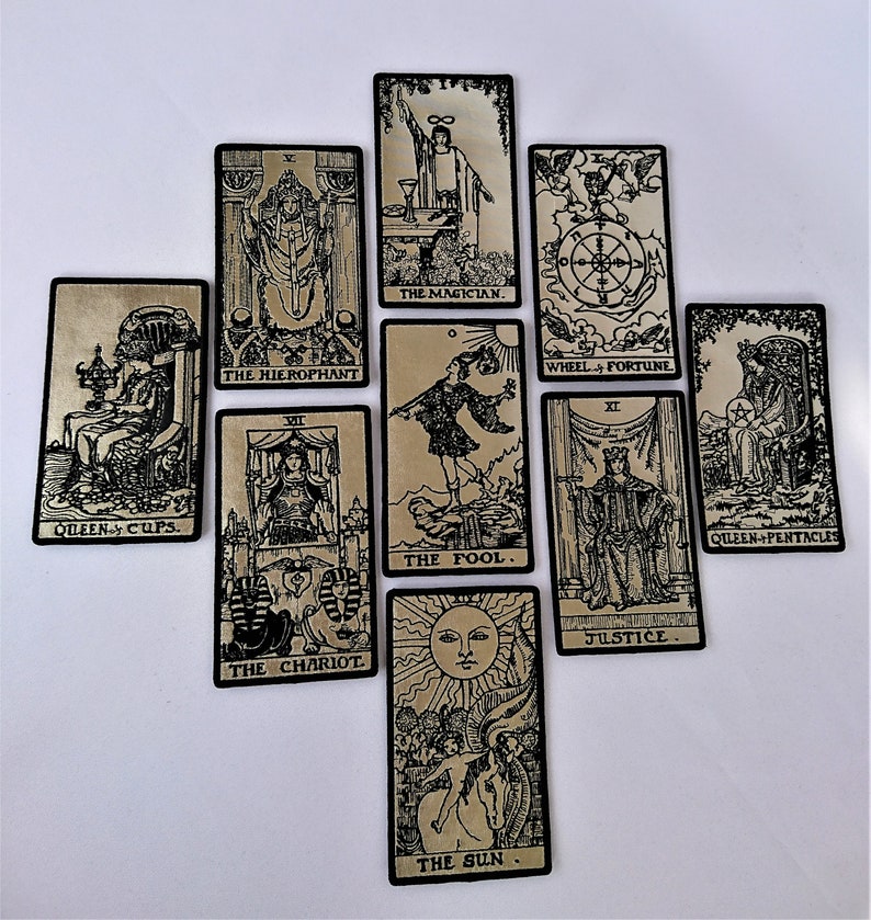 May include: A set of ten tarot cards with black and white illustrations on a gold background. The cards include The Magician, The Hierophant, The Chariot, The Fool, The Sun, Wheel of Fortune, Justice, Queen of Cups, Queen of Pentacles.