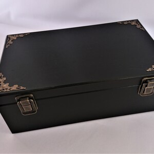 May include: A black wooden box with ornate brass corner accents and two brass clasps. The box has a hinged lid.
