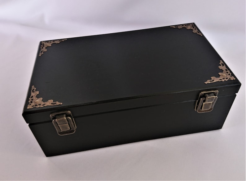May include: A black wooden box with ornate brass corner accents and two brass clasps. The box has a hinged lid.