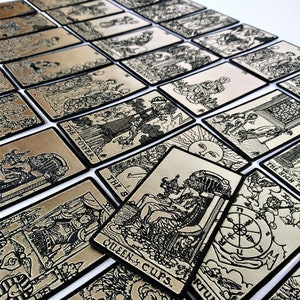 May include: A set of 22 tarot cards with black and white illustrations on a gold background. The cards are arranged in a staggered pattern, with the top card showing the Queen of Cups. The cards are made of a thick, durable material and have a black border.