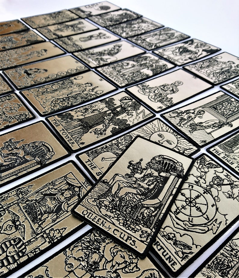 May include: A set of 22 tarot cards with black and white illustrations on a gold background. The cards are arranged in a staggered pattern, with the top card showing the Queen of Cups. The cards are made of a thick, durable material and have a black border.