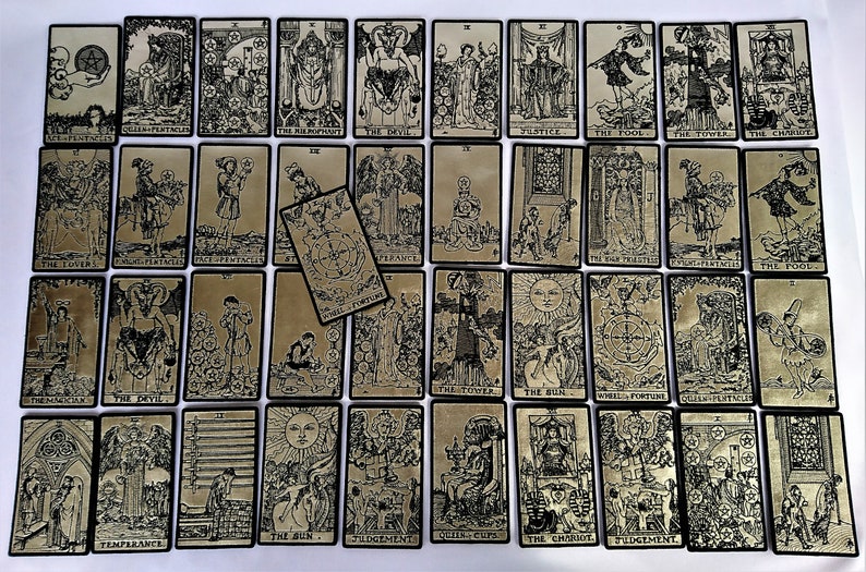 May include: A full deck of tarot cards with black and white illustrations on a gold background. The cards are arranged in rows and columns, with the backs of the cards facing up. The cards are numbered from 1 to 22, and each card has a different illustration.